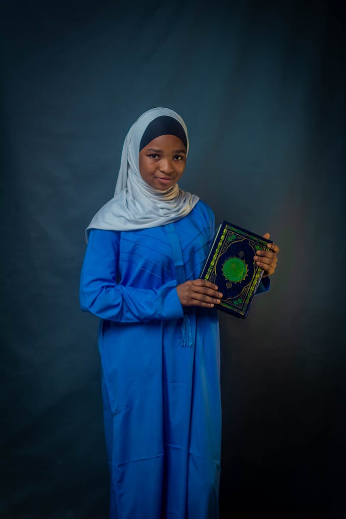 Portrait of a young girl in traditional attire holding the Quran, symbolizing faith and education.