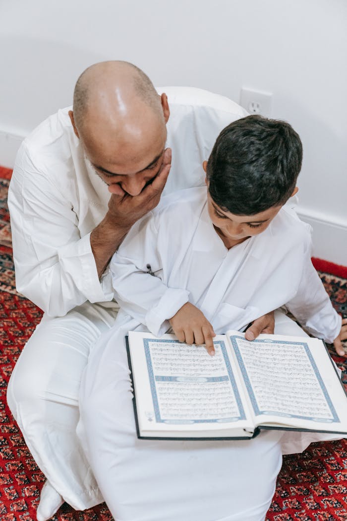 Father and son bonding while reading the Quran, fostering cultural and religious learning.